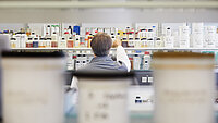 Lab technician reaching for a bottle on a shelf filled with labeled chemical containers.